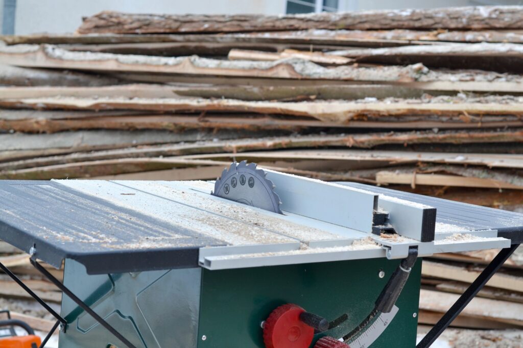 Electric table saw outdoors with large stacks of timber in the background